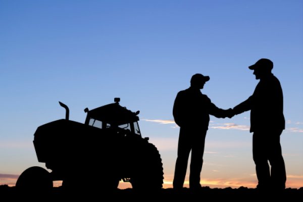 A royalty free image from the farming industry of two farmers shaking hands in front of a tractor.